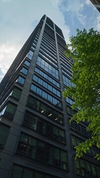 Wide angle dolly camera movement looking up modern office tower business building with blue sky reflections, skyscraper in financial district, architecture and success concept