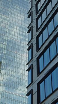 Low angle smooth cinematic dolly movement between modern glass skyscrapers in business district, corporate architecture, urban growth, financial success and contemporary city development