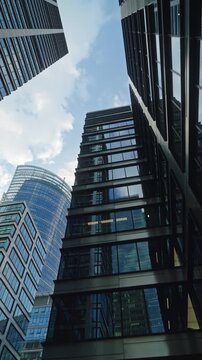 Low angle smooth cinematic dolly movement between modern glass skyscrapers in business district, corporate architecture, urban growth, financial success and contemporary city development