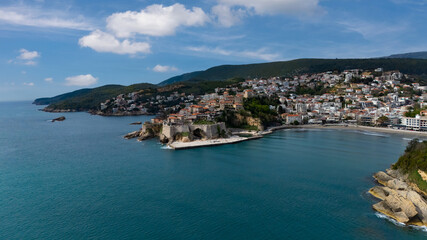 Fototapeta premium Captivating aerial shot of the historic stone citadel of Ulcinj, perched on a rocky peninsula alongside a sweeping sandy beach bay and deep blue sea.