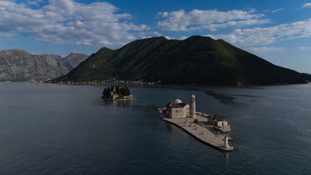 Stunning drone shot of the iconic islets, Our Lady of the Rocks and Saint George, floating in the calm waters of Perast bay, framed by dramatic coastal mountains.