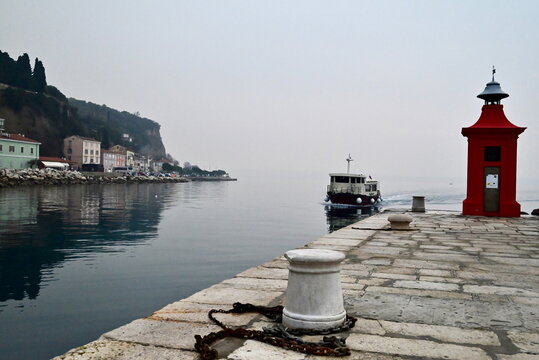 Cinematic red lighthouse at Piran harbor pier with passenger ferry boat arrival Slovenia travel.