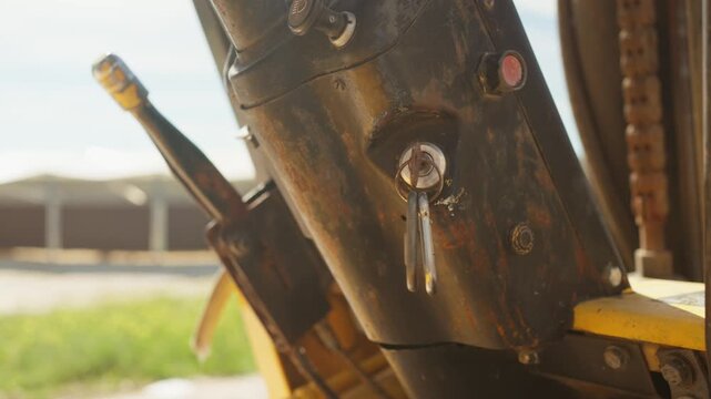 Closeup of forklift ignition key inserted in mechanical control system with metal texture and sunlight reflections. Detailed agricultural machinery