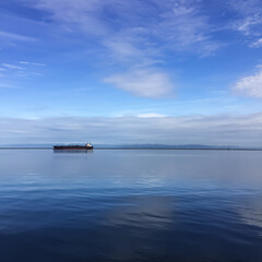 Obraz premium water with sunny cloudy skies and boat near horizon line