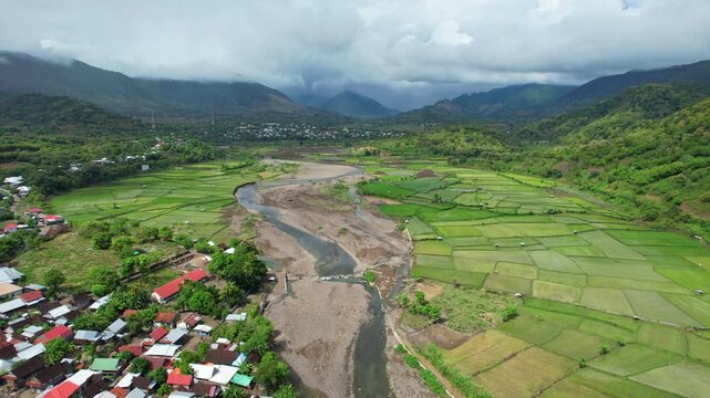 Aerial drone footage of Rite village and river in the middle of a beautiful watery rice field valley, with its mosque, in cloudy weather, in Bima area, Sumbawa island, Indonesia