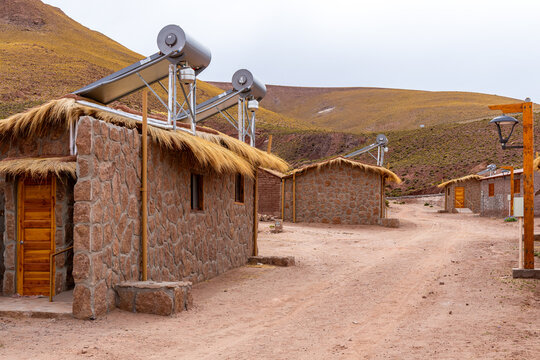 View of traditional stone houses with thatched roofs and solar water heaters along a dirt path in the Andean highlands Machuca, Antofagasta, Chile.