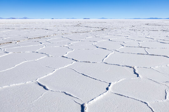View of Uyuni Salt Flat with hexagonal salt crust patterns stretching towards distant mountains under a clear blue sky Potosi Department, Bolivia.