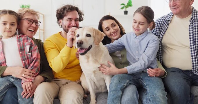 Family grandparents parents children bonding with labrador dog. They sit together at home, smiling, petting the pet and talking, enjoying time. Warm multigenerational connection at home.