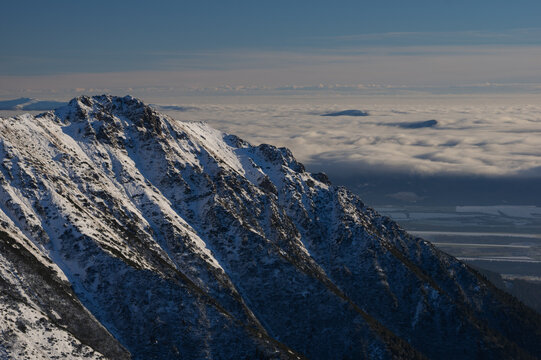 View of Koncisty Vrch in Western Tatras featuring snow-covered rocky ridges above a sea of clouds in Pribylina, Zilinsky kraj, Slovakia.