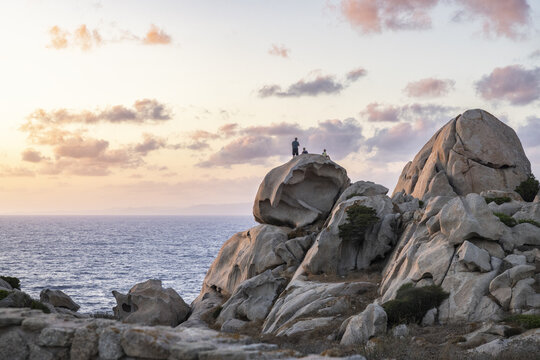 View of the granite rock formations of Capo Testa with people standing on top during a soft sunset over the Mediterranean Sea in Capo Testa, Sardegna, Italy.