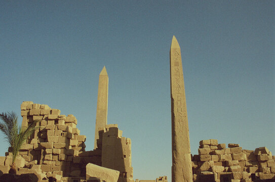 Two Egyptian Obelisks Rising Above Karnak Temple Ruins with Palm Tree
