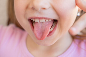 Teasing or joking gesture used kids express silliness, closeup little girl sticking tongue out, playful naughty expression, pink shirt, macro shot mouth and nose, funny childhood emotion, skin texture © kittyfly