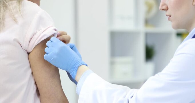Doctor in medical gloves applying adhesive bandage onto patient's arm after vaccination in hospital, closeup