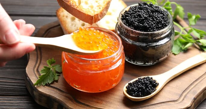 Woman putting delicious red caviar on bread slice at wooden table, closeup