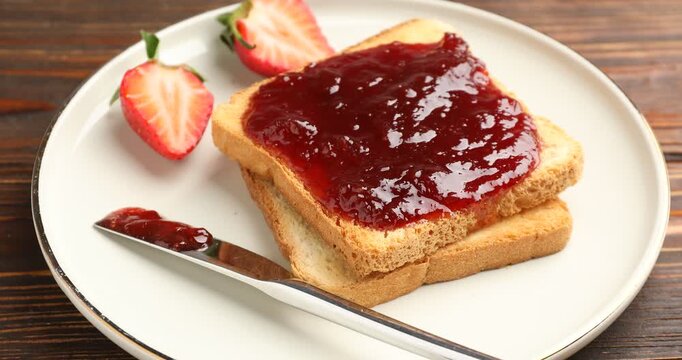 Slices of toasted bread with strawberry jam on wooden table, camera zooming