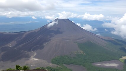 Fototapeta premium Majestic Volcanic Mountain Peak with Lush Green Forest Under Dramatic Cloudy Sky