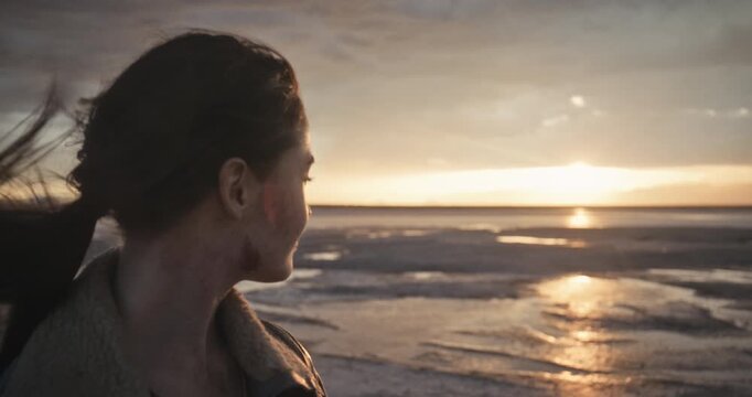 Smiling woman covered in dirt staring out at sunset over wet desert - slow motion moving shot