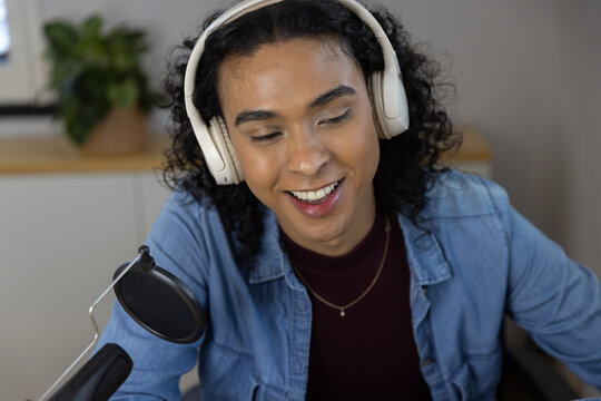 Non-binary person wearing denim shirt recording with microphone and white headphones at home studio