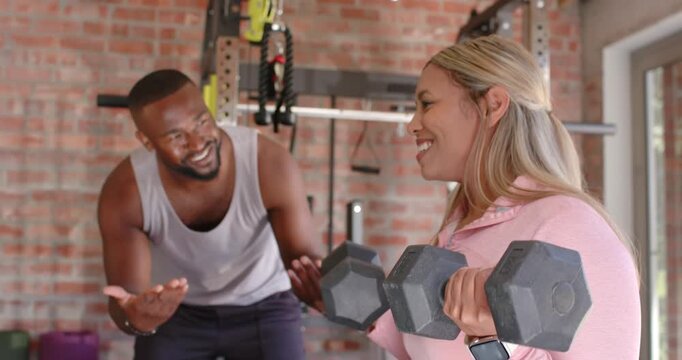 African American client following trainer cue doing seated curls with dumbbells at gym for strength