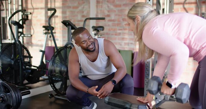 African American trainer and client in sportswear at bench, trainer cueing dumbbell rows for form