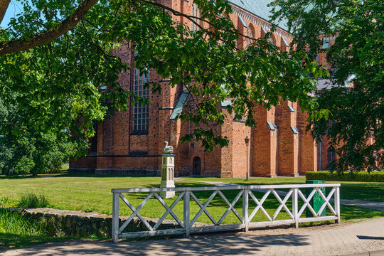 Bad Doberan, Germany - 19 July 2025: View of the Doberaner Munster with its red brick Gothic architecture partially framed by green trees and a white wooden fence.