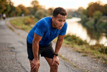 Fototapeta premium Exhausted male runner resting with hands on knees after jogging