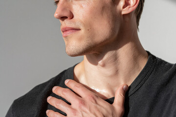 Fototapeta premium Young man hand on collarbone in sunlight, closeup skin texture, jawline, neck, casual gesture