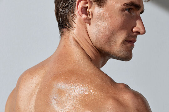 Glowing male shoulder and upper back with water droplets under soft daylight, athletic skin texture and relaxed pose conveying freshness and healthy vitality