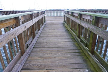 Obraz premium A first-person perspective view walking on a weathered wooden boardwalk structure or pier over water. The pathway is lined with heavy wooden safety railings leading to an open deck viewpoint area unde