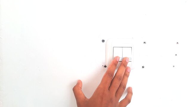 Close up of an Asian man hand turning on a white wall light switch in a minimalist workspace. Young male finger pressing the button to switch on the lights, initiating work or saving energy concept. 