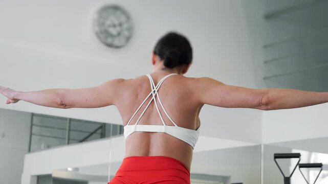 Rear view of woman performing Pilates balance exercise on reformer machine in bright studio, flexibility and posture workout.