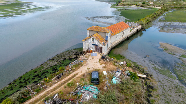 Alhos Vedros, Portugal - 16 December 2024: Aerial view of a historic tide mill building with an orange tiled roof situated on a narrow pier along the Tagus River estuary.