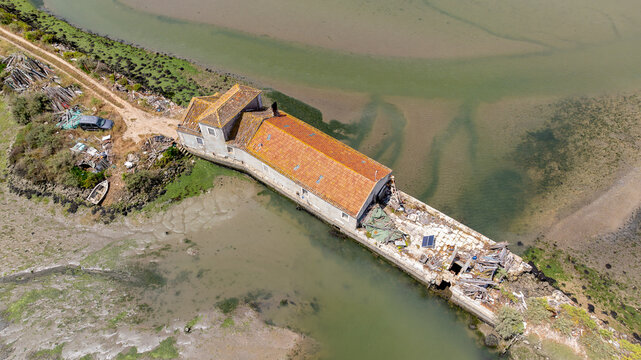 Alhos Vedros, Portugal - 16 December 2024: Aerial view of a historic tide mill building with a terracotta roof situated on the mudflats of the Tagus river estuary.