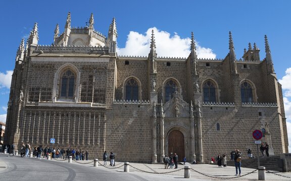 Large Gothic church with stone walls and towers under a blue sky, people standing in front of it, Monasterio de San Juan de los Reyes, Toledo, Castilla-La Mancha, Spain