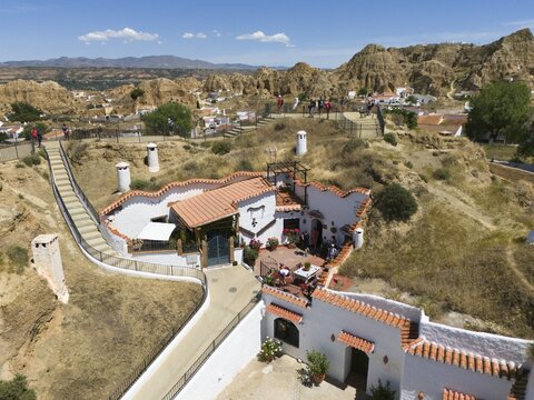 A white house with terracotta roof on a hill surrounded by nature and some people enjoying the scenery, aerial view, cave dwellings, cave neighbourhood, Troglodytos, Guadix, Granada, Andalusia, Spain