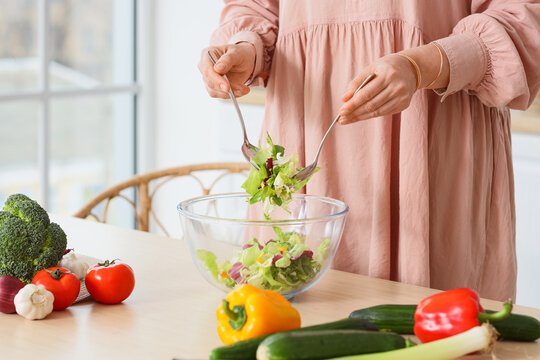 Woman making vegetable salad at table in kitchen, closeup