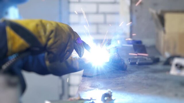 Close up of industrial worker welding metal with bright sparks in workshop. Heavy industry and metal fabrication process indoors.