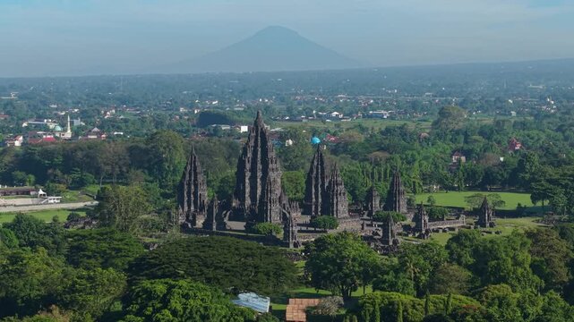 Aerial view of the ancient Prambanan Temple complex surrounded by lush green trees with Mount Merapi in the distance Kecamatan Prambanan, Daerah Istimewa Yogyakarta, Indonesia.
