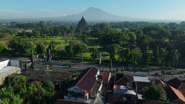 Aerial view of Prambanan Temple complex with Mount Merapi in the background and residential rooftops in the foreground in Kecamatan Prambanan, Daerah Istimewa Yogya, Indonesia.