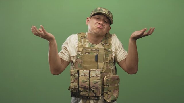 Man in camouflage military uniform shrugs hands palms up wearing tactical vest and dogtag in studio; confusion.