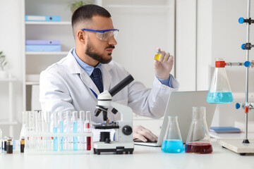 Fototapeta premium Male scientist with ampule and laptop working in laboratory