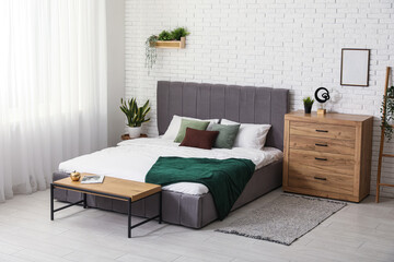 Comfortable bed and chest of drawers near white brick wall in interior of bedroom