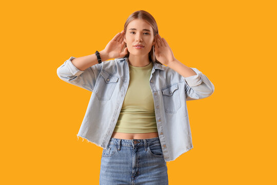 Young woman trying to hear something on yellow background