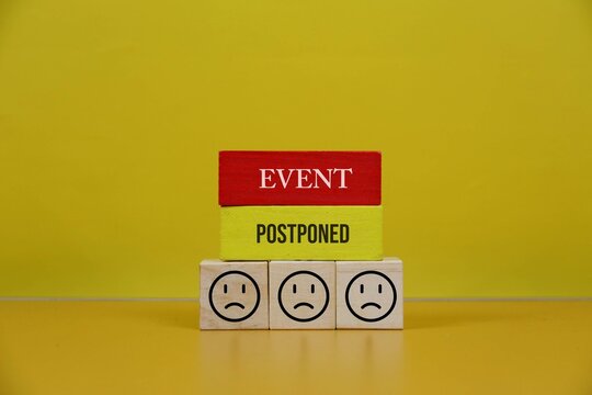 Postponed Event Announcement With Wooden Blocks and Sad Faces Representing Cancellation and Disappointment, with an yellow background.