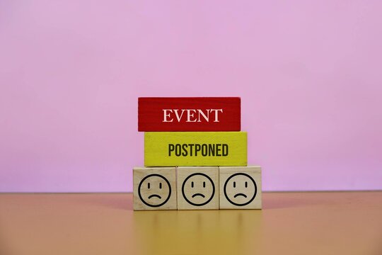 Postponed Event Announcement With Wooden Blocks and Sad Faces Representing Cancellation and Disappointment, with an pink background.