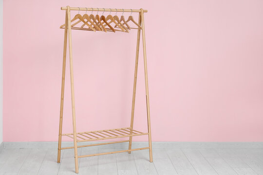 Wooden rack with hangers near pink wall