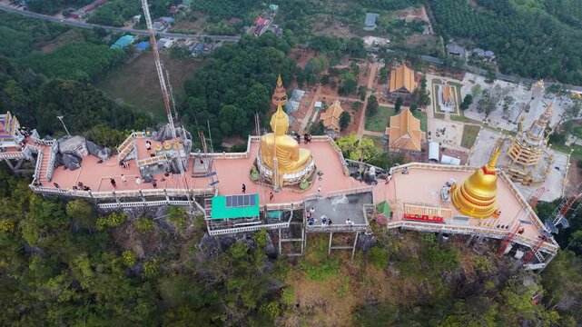 Krabi Noi, Thailand - 24 May 2026: Aerial view of the large golden Buddha statue at Tiger Cave Temple viewpoint with tourists and lush tropical landscape.