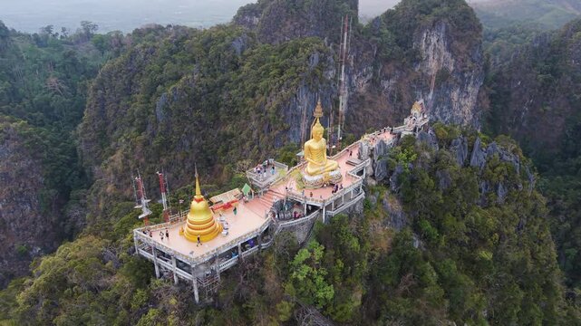 Krabi Noi, Thailand - 24 May 2026: Aerial view of the Viewpoint at Tiger Cave Temple featuring the golden Buddha statue and stupa atop limestone cliffs surrounded by lush forest.