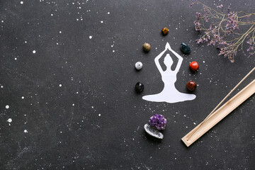 Naklejka premium Set of chakra stones, incense, flowers and paper figure of meditating human on dark background