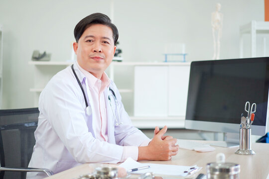 Smiling asian doctor sitting in modern clinic office